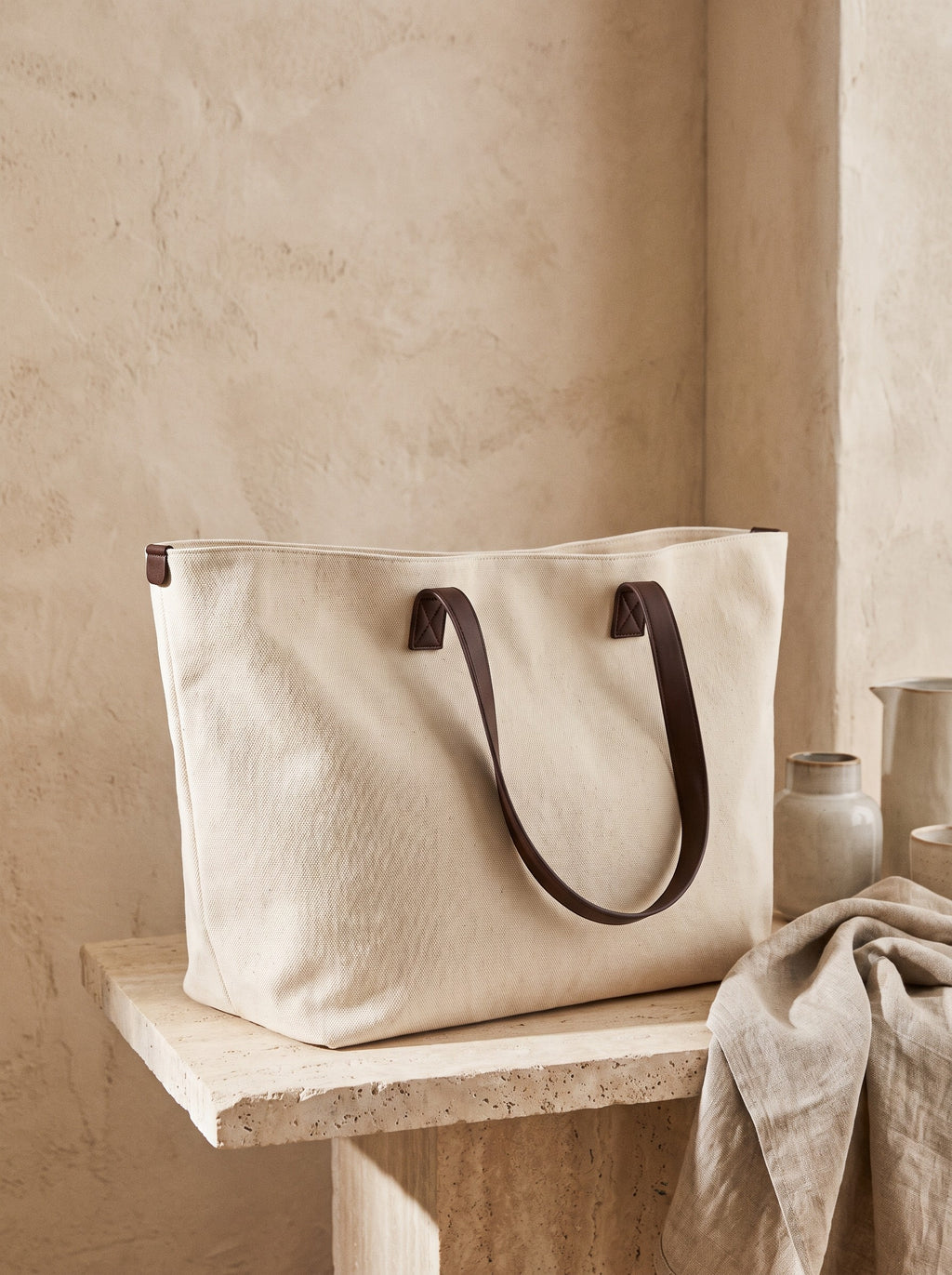 Canvas Weekend Tote in natural cotton canvas with brown handles on a stone plinth