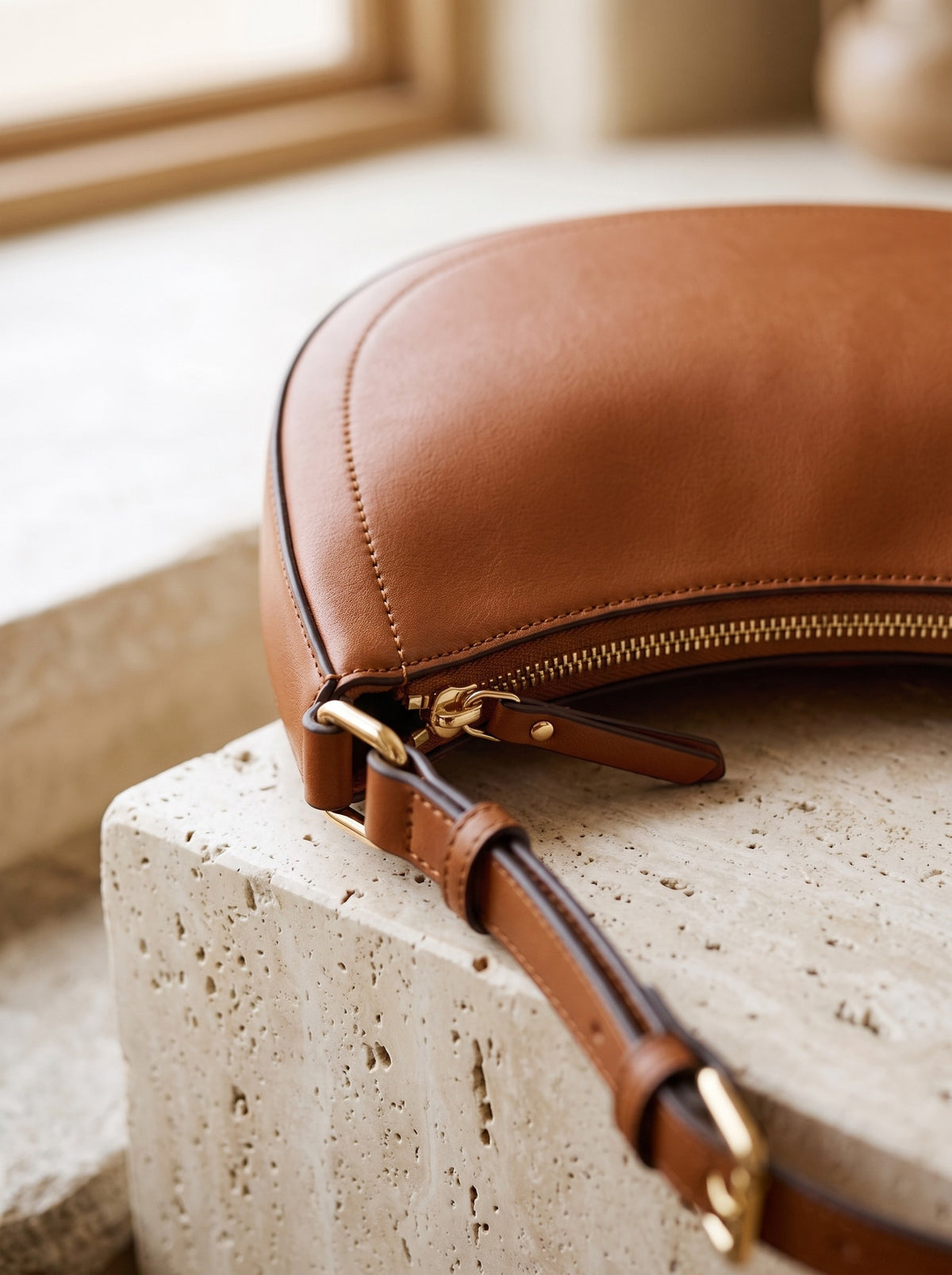 Close-up of the gold-tone zip and strap buckle on the cognac Crescent Shoulder Bag