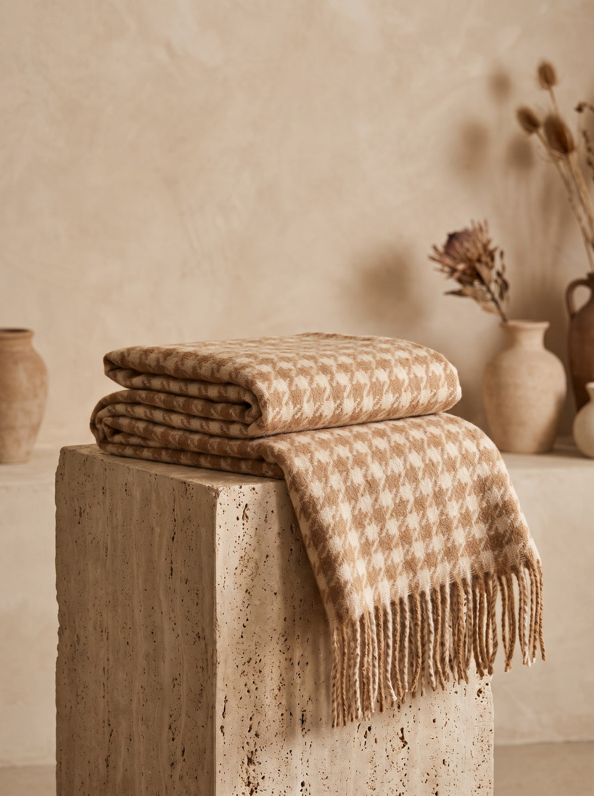 Houndstooth Blanket Scarf in camel and cream folded on a travertine plinth