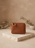 Mini Zip Coin Purse in cognac vegan leather with a key ring clip on a travertine block