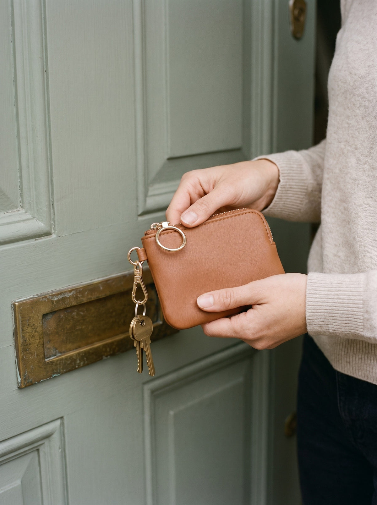 Hands holding the cognac Mini Zip Coin Purse clipped to a set of keys