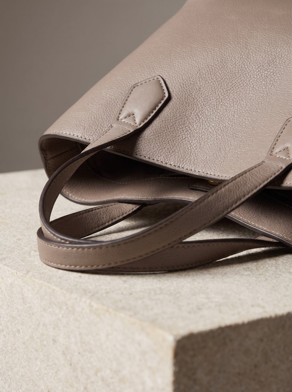 Close-up of the stitched handle tabs and grained surface of the taupe Structured Mini Tote