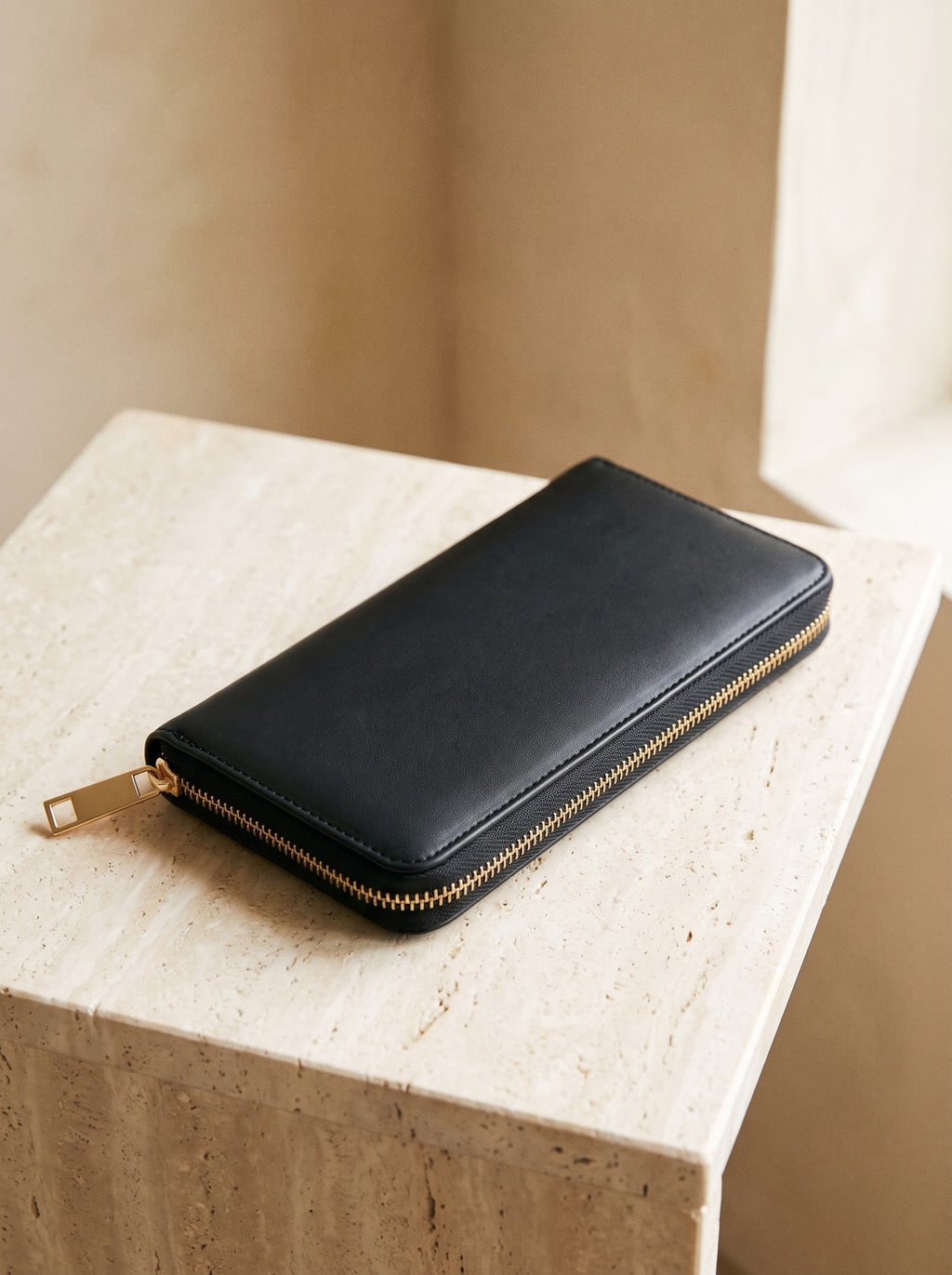Zip-Around Wallet in black vegan leather lying on a travertine block