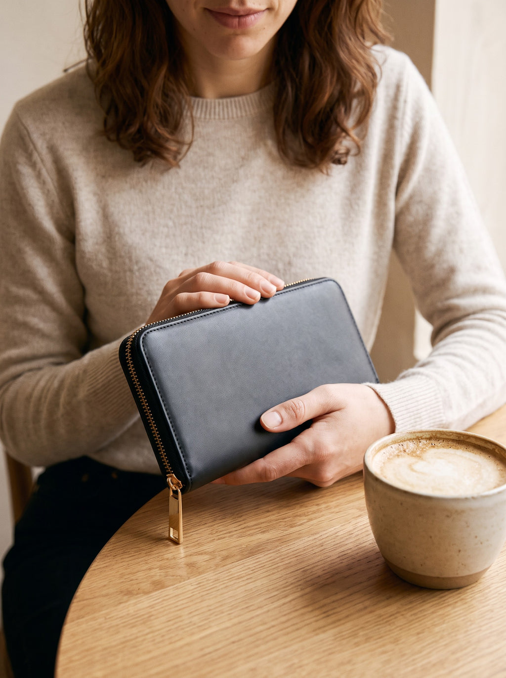 Woman holding the black Zip-Around Wallet at a cafe table